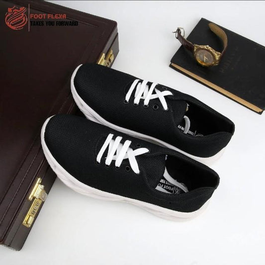Black sneakers with white laces on a white surface, with a briefcase and watch in the background.