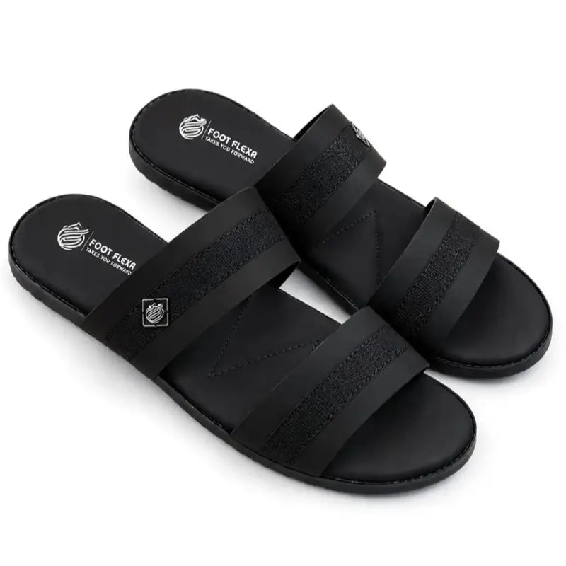 A pair of black slide sandals with wide double straps, featuring a textured velcro-style upper and a contoured footbed with the brand name 'FOOT FLEX' printed in white.