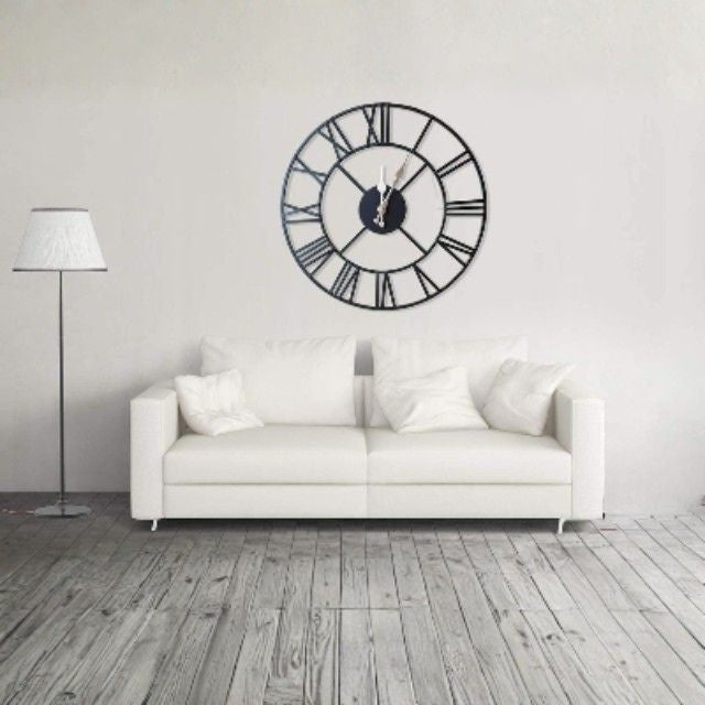 Large black wall clock on a white wall above a white sofa.