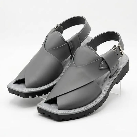A pair of dark gray leather slingback sandals with chunky lug soles, displayed on a clear acrylic riser against a white studio background.