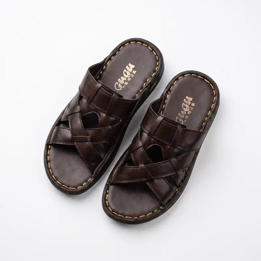A pair of dark brown leather slide sandals with woven crisscross straps and contrast stitching, displayed on a clean white background. The brand name 'CAGIA' is visible on the footbed.