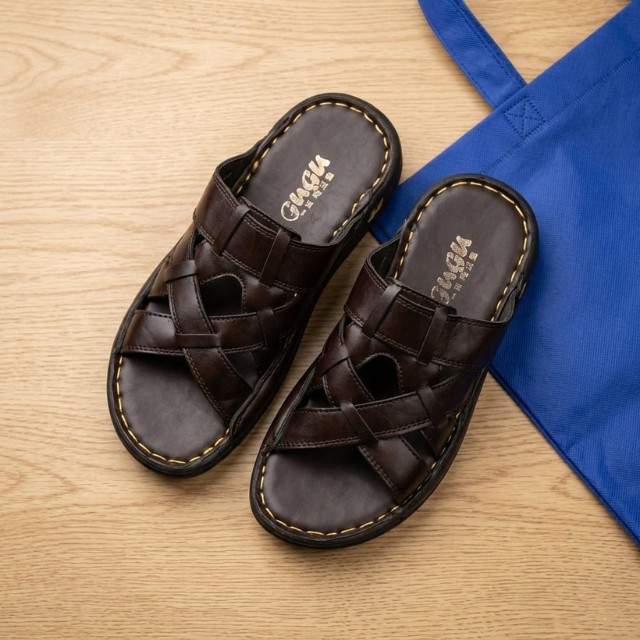 Pair of brown sandals on a wooden surface with a blue bag in the background