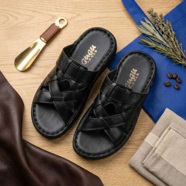 Black sandals with woven design on a wooden surface with a shoe horn and herbs.