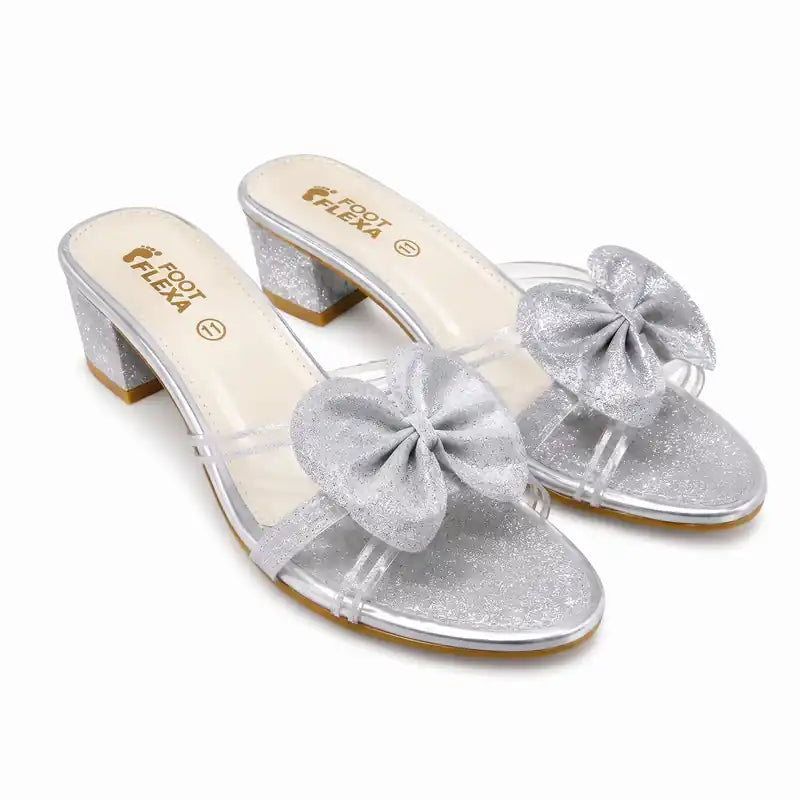 A pair of women's heeled mule sandals in silver glitter, featuring a chunky block heel, clear straps, and a large glittery bow on the toe area. The brand name 'FEBA' is printed on the insole.